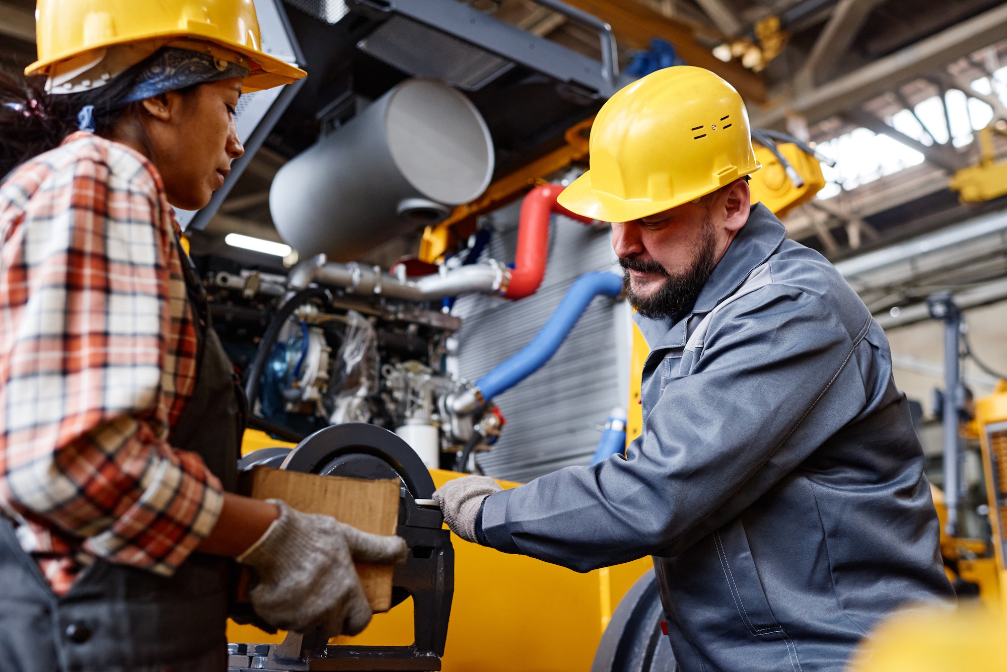 mature workman in hardhat and workwear fixing shaft of industrial machine